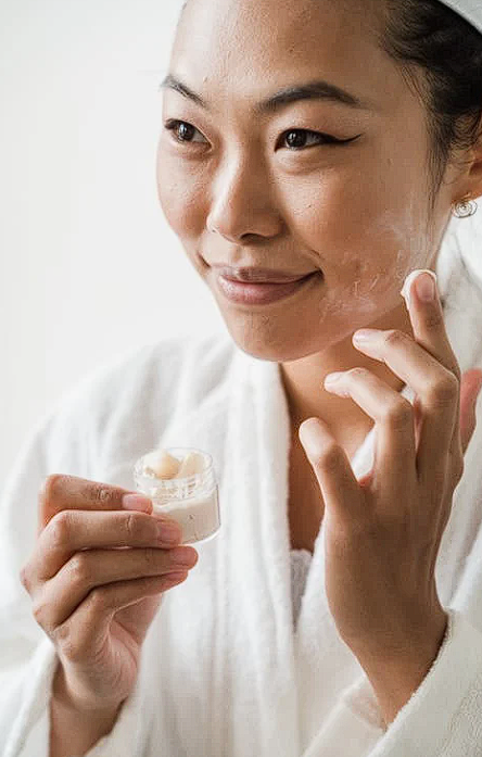 Femme souriante en peignoir appliquant une crème hydratante sur le visage, routine beauté lumineuse du matin