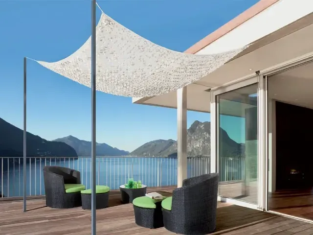 Terrasse contemporaine avec voile d’ombrage ajourée, mobilier en rotin noir et vue panoramique sur un lac entouré de montagnes.