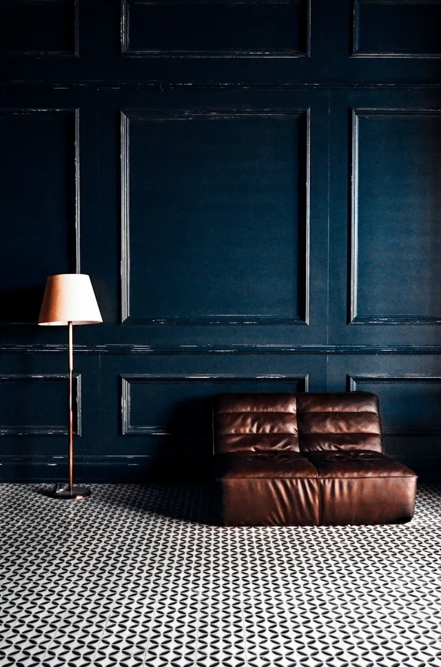 Coin lecture minimaliste avec fauteuil en cuir brun, mur bleu nuit à moulures et sol graphique noir et blanc