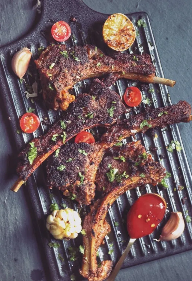 Côtelettes d’agneau grillées avec tomates cerises, ail rôti, citron grillé et sauce rouge épicée sur planche en fonte striée