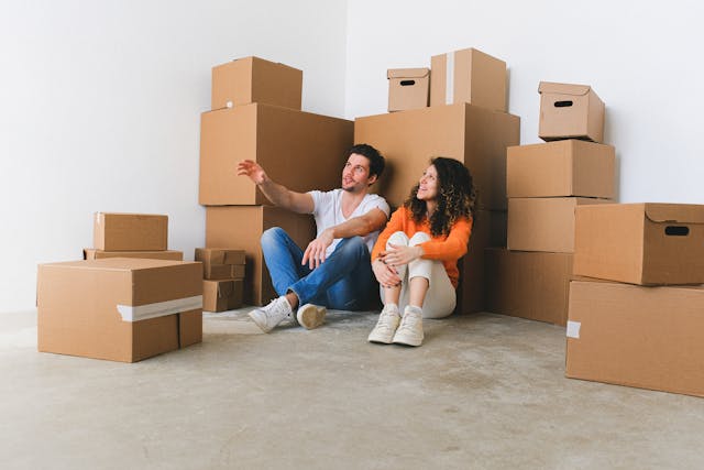 Jeune couple assis au sol au milieu de cartons de déménagement, ambiance complice et début de nouvelle vie à deux