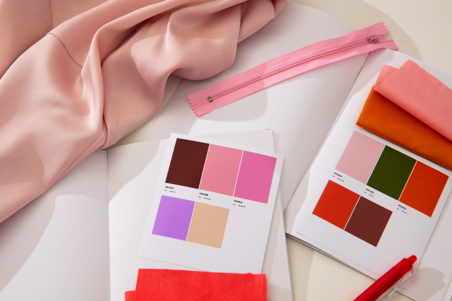 Échantillons de tissus dans des tons rose et orange, accompagnés de nuanciers et d’une fermeture éclair assortie