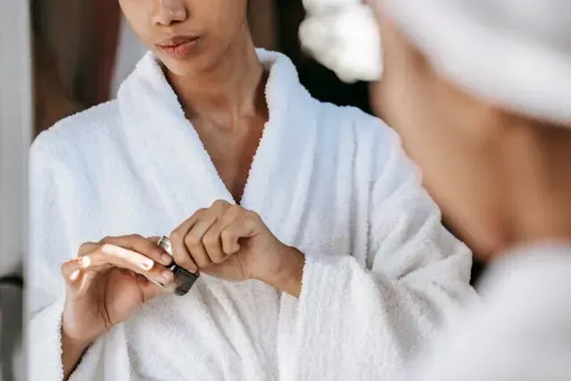 Femme en peignoir ouvrant un flacon de soin devant le miroir, moment calme d’une routine beauté du matin