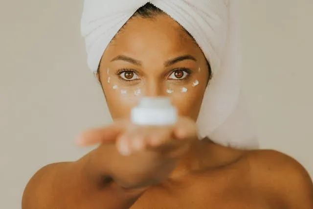 Femme avec serviette enroulée sur la tête appliquant un soin contour des yeux, geste beauté ciblé et lumineux du matin