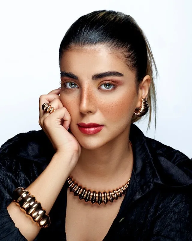 Femme au maquillage affirmé avec lèvres rouges, taches de rousseur et bijoux dorés sculpturaux, posant en studio