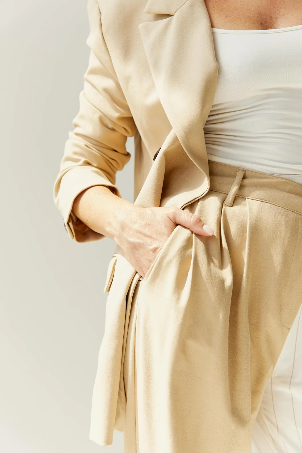 Femme en tailleur beige clair avec veste fluide et top blanc, debout avec la main glissée dans la poche du pantalon