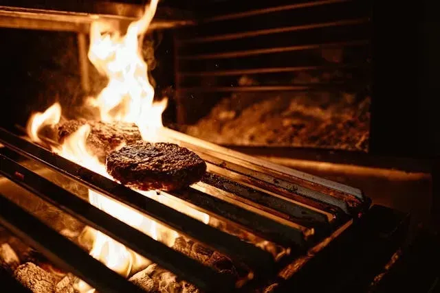 Galettes de viande grillées au feu de bois, cuisson directe sur flammes vives dans un foyer traditionnel