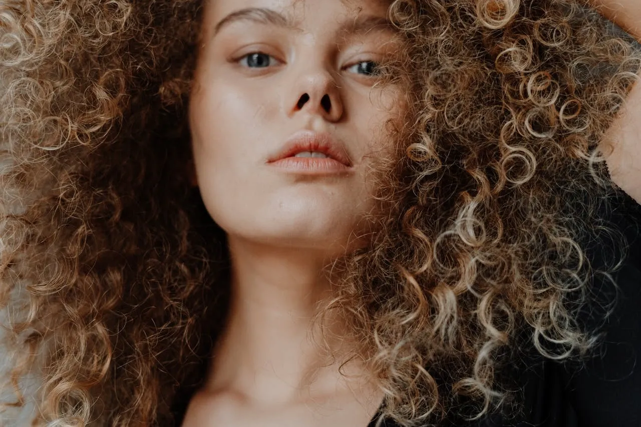 Gros plan sur une femme aux cheveux très bouclés, regard direct et expression authentique