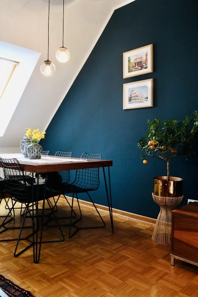 Salle à manger scandinave avec mur bleu profond, table en bois clair, suspension globe et parquet lumineux