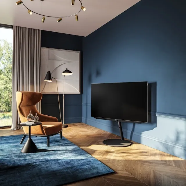 Salon contemporain avec mur bleu clair, fauteuil design cognac, grande baie vitrée et écran TV sur pied