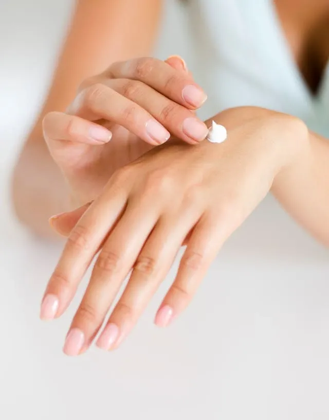 Application délicate de crème hydratante blanche sur le dos de la main, peau douce et ongles soignés en gros plan