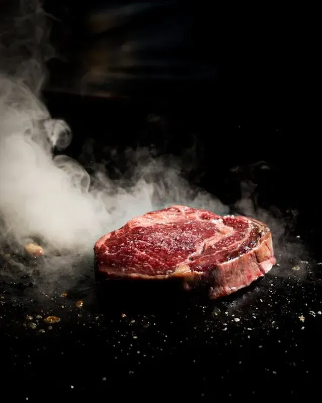 Viande rouge saisie à la plancha avec fumée visible sur fond noir