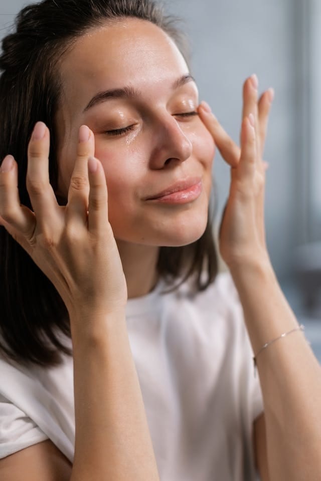 Femme massant son visage avec une crème hydratante, yeux fermés et expression détendue