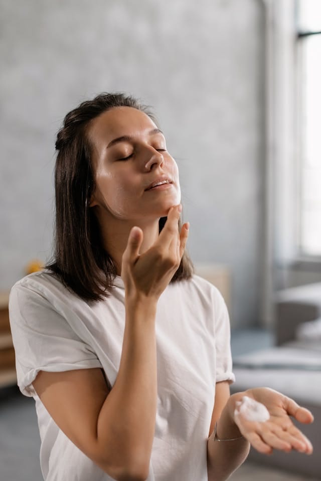 Femme appliquant de la crème hydratante sur son visage, moment de soin apaisant en intérieur