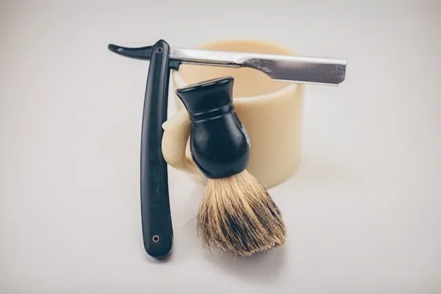 Accessoires de rasage traditionnel avec blaireau, coupe-chou et savon sur support clair, esprit vintage masculin