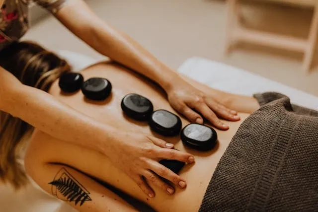 Massage relaxant aux pierres chaudes sur le dos d’une femme, dans un institut à l’ambiance douce et enveloppante
