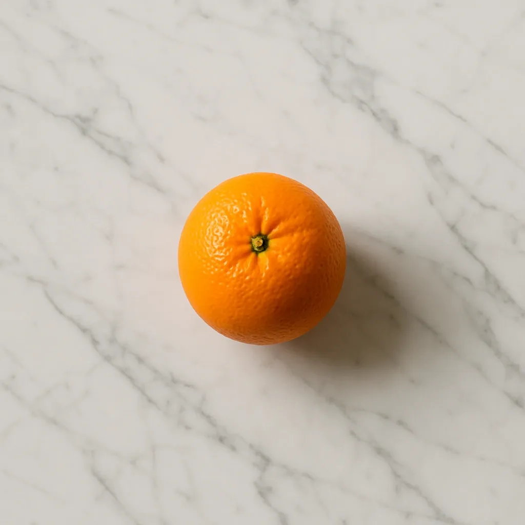 Orange posée sur un plan de travail en marbre clair veiné, composition minimaliste et naturelle en cuisine