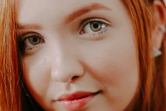 Portrait d’une femme aux cheveux roux avec un maquillage naturel et un regard doux, idéal pour illustrer un article beauté ou sourcils.