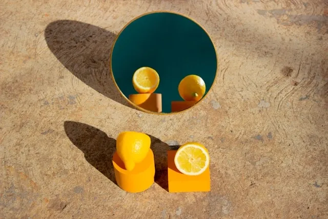 Citron jaune coupé reflété dans un miroir rond au sol, composition graphique avec formes géométriques