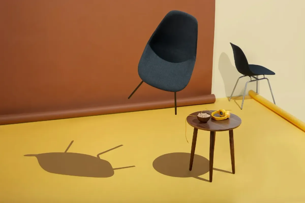 Chaise design bleu foncé suspendue dans un studio coloré avec sol jaune et mur brun, table en bois.