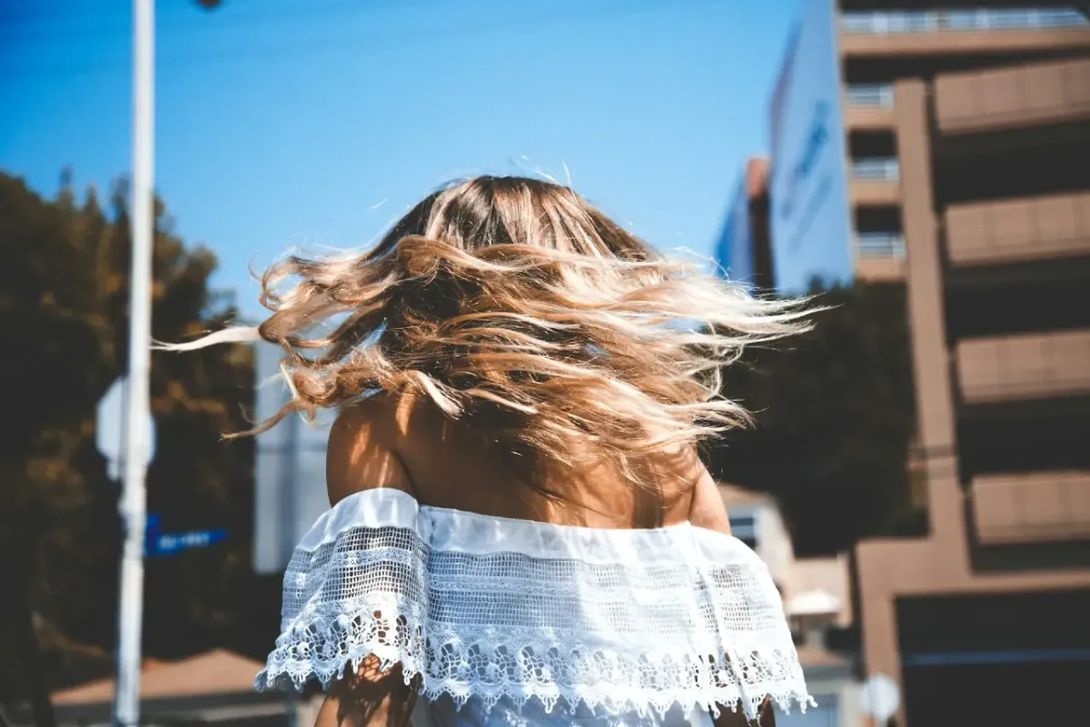 Femme en robe d’été blanche de dos, cheveux au vent dans une rue ensoleillée