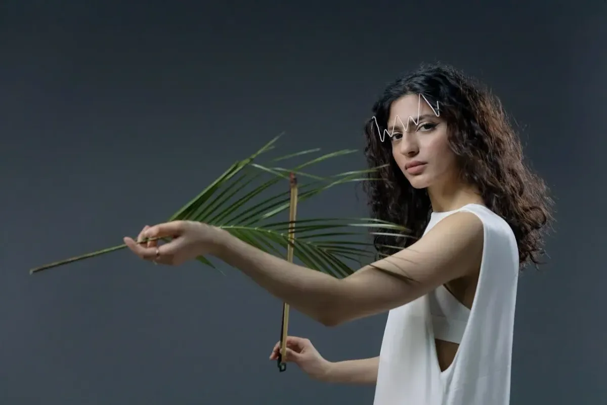 Femme au style moderne tenant une feuille de palmier dans un studio sur fond gris, look artistique et minimaliste