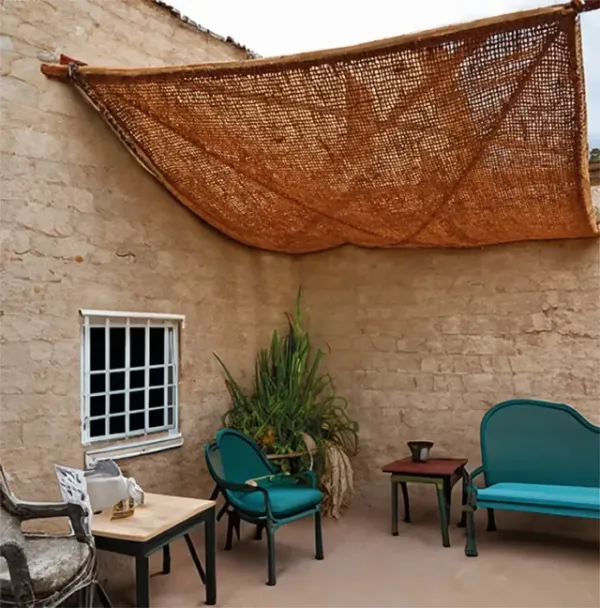 Terrasse intérieure en pierre beige avec voile d’ombrage en fibre naturelle et mobilier bistrot aux accents vintage.