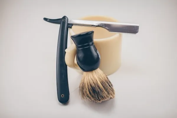 Accessoires de rasage traditionnel avec blaireau, coupe-chou et savon sur support clair, esprit vintage masculin