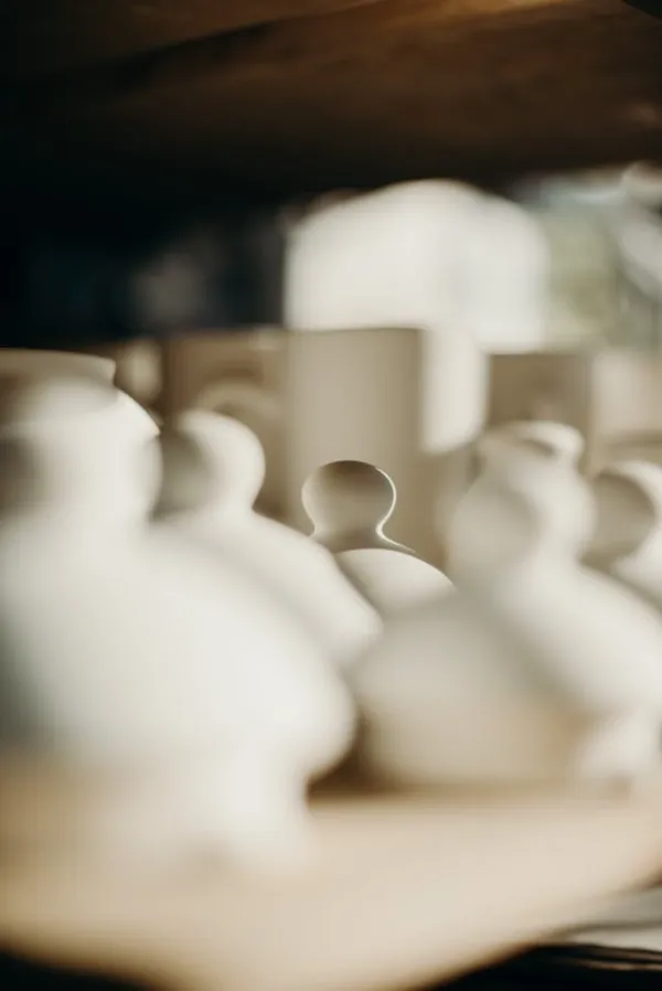 "Pièces en céramique blanche floutées sur une étagère en bois dans un atelier de poterie artisanal au repos