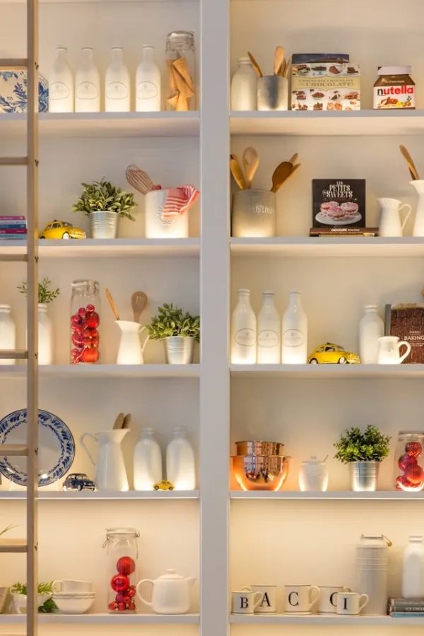 Étagère de cuisine blanche décorée avec bocaux en verre, vaisselle blanche, plantes vertes et objets vintage en lumière naturelle