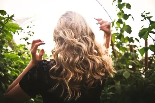Femme blonde de dos aux cheveux ondulés, captée en pleine lumière naturelle dans un jardin luxuriant