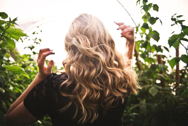 Femme blonde de dos aux cheveux ondulés, captée en pleine lumière naturelle dans un jardin luxuriant