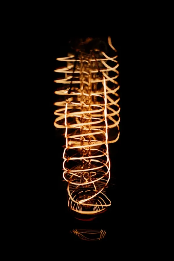 Gros plan sur un filament incandescent allumé, spirale lumineuse dorée sur fond noir profond