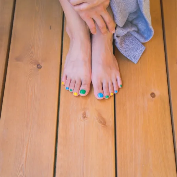 Pieds vernis multicolores posés sur une terrasse en bois, ambiance estivale et détente au soleil
