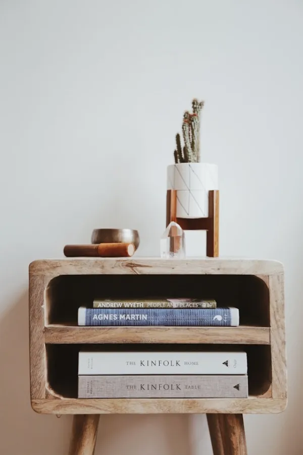 Table de chevet en bois brut avec livres Kinfolk empilés, cactus dans un pot en céramique et décoration minimaliste