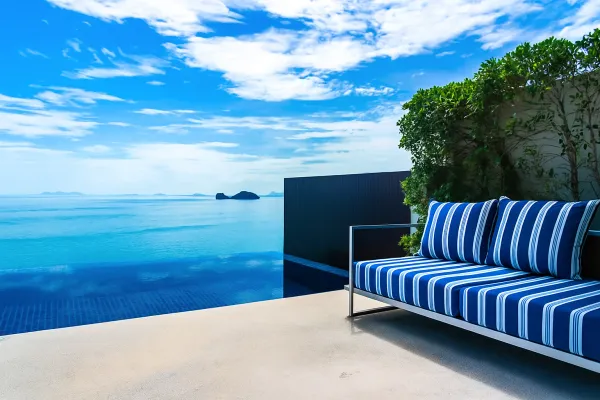 Terrasse élégante en bord de mer avec canapé rayé bleu et blanc, piscine à débordement et vue dégagée sur un horizon insulaire