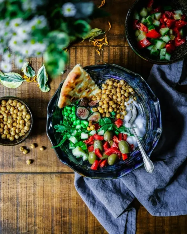 Assiette végétarienne colorée vue de dessus avec pois chiches, crudités, pain plat et sauce, sur bois brut