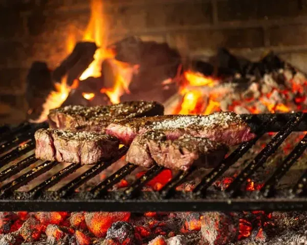 Morceaux de bœuf grillés au gros sel sur braise ardente, en pleine cuisson dans un foyer traditionnel avec flammes vives