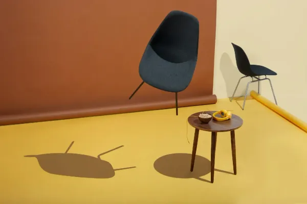 Chaise design bleu foncé suspendue dans un studio coloré avec sol jaune et mur brun, table en bois.