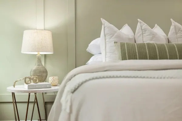 Chambre lumineuse avec lampe en rotin, linge de lit blanc et coussin vert rayé, décoration naturelle.
