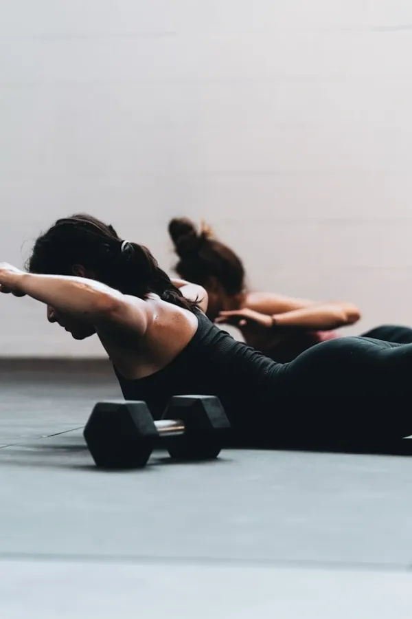 Femmes en tenue noire réalisant un gainage au sol dans une salle de sport, effort collectif et concentration