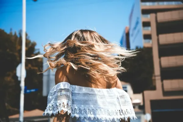 Femme en robe d’été blanche de dos, cheveux au vent dans une rue ensoleillée