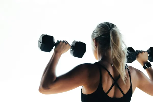 Femme sportive s’entraînant avec haltères, vue de dos en tenue de fitness.