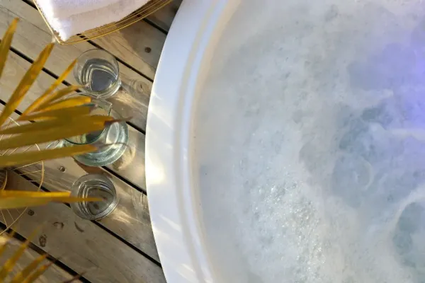 Bord de jacuzzi encastré sur terrasse en bois, deux verres d’eau posés, ambiance spa lumineuse et apaisante