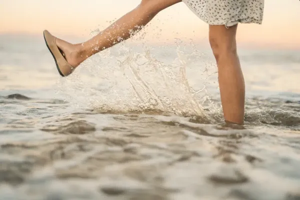 Femme marchant dans l’eau au bord de la mer, éclaboussures au coucher du soleil