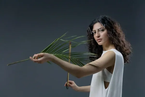 Femme au style moderne tenant une feuille de palmier dans un studio sur fond gris, look artistique et minimaliste