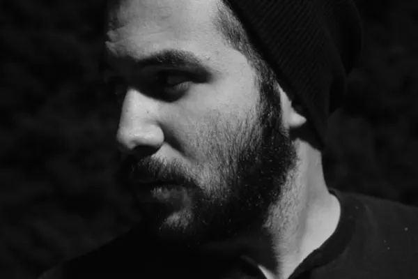 Portrait en noir et blanc d’un homme barbu portant un bonnet, regard vers la gauche, éclairé en clair-obscur