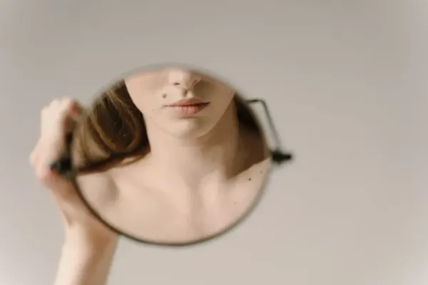 Portrait artistique d’une femme tenant un miroir reflétant partiellement son visage et son décolleté