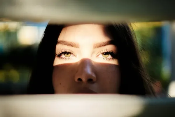 Regard intense d’une femme aux yeux verts observant à travers des stores partiellement ouverts
