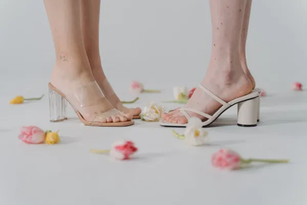 Pieds de femmes portant des sandales à talons tendance sur fond blanc décoré de fleurs